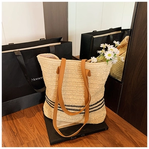 Détail d'un sac cabas en paille tissé avec rayures noires et anses en cuir brun