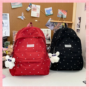 Close-up of floral canvas backpacks in red and black with plush pendant and brand label