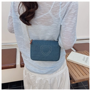 Detail of blue denim crossbody bag with heart embroidery and silver chain strap