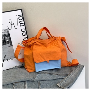 Détail du sac cabas en nylon orange montrant la poche avant bleu clair et la bandoulière