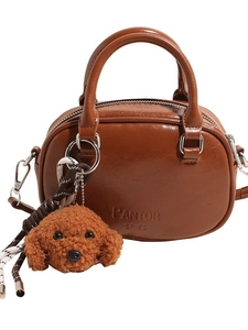 Brown leather handbag with round silhouette and curly poodle plush charm on pure white background