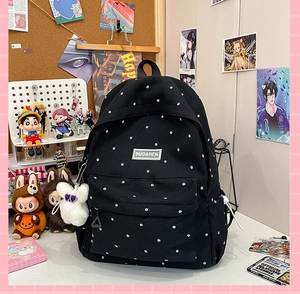 Detail of black backpack with white floral patterns and a plush bunny charm on desk
