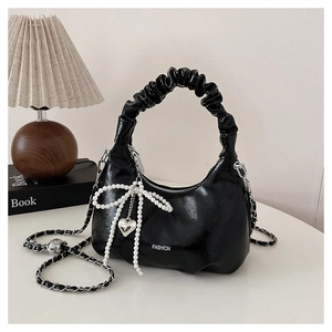 Detail of black glossy handbag with pleated handle, pearl bow and silver heart charm
