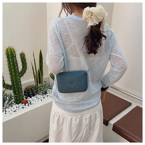 Detail of blue denim heart embroidery crossbody bag with silver chain strap on model