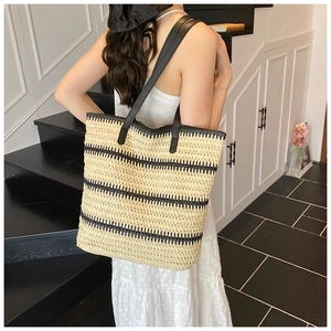 Détail du sac cabas en paille tressée avec rayures noires et anses en cuir sur modèle
