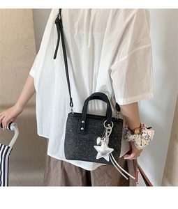 Detail of black sequin bucket bag with silver star and heart charms worn as a crossbody