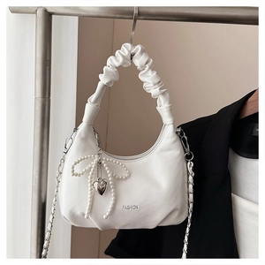 Detail of white half-moon bag with pleated handle, pearl bow and silver heart pendant