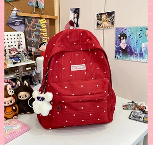 Close-up of red polka dot backpack with a white plush bear charm on a desk