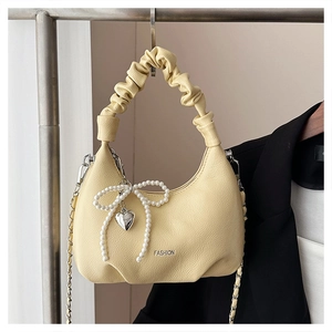 Detail view of yellow pleated bag with pearl bow, heart charm and fashion print