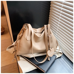 Detail of soft pleated beige shoulder bag with heart-shaped charm and delicate strap