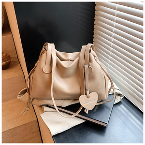 Close-up of beige pleated bucket bag featuring heart charm and slim shoulder straps