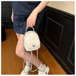Close-up of beige quilted mini backpack with silver twist lock and woven chain strap