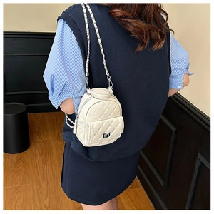 Detail of a quilted cream mini backpack with a metal chain strap shown from the back view