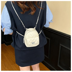Rear view of a beige quilted mini backpack with silver chain strap worn by a model