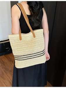 Sac fourre-tout en paille avec rayures noires et anses en cuir porté par un mannequin