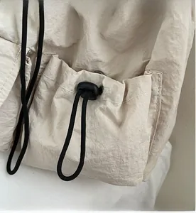 Detail der cremeweißen Canvas-Tasche mit plissiertem Stoff und schwarzem Kordelzugverschluss