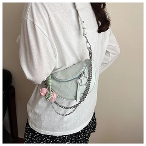 Detail of mint green crescent saddle bag with silver chains and woven charm on a model