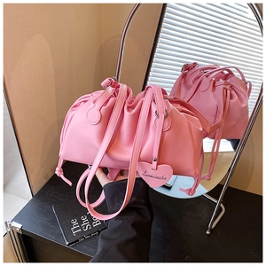 Detail of pink pleated crossbody bucket bag with heart pendant and drawstring accents