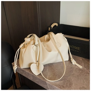 Detail of creamy white pleated crossbody bag with heart charm on marble surface