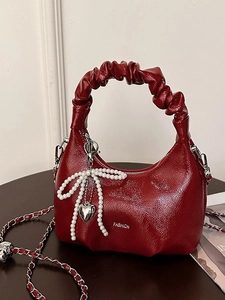 Chic burgundy pleated dumpling bag with pearl bow and chain strap on a dark table
