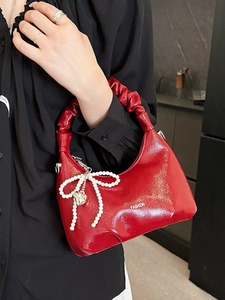 Red glossy patent leather handbag with pleated handle and pearl bow charm shown by model