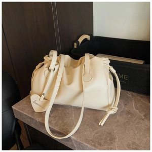 Detail of cream pleated cloud bag featuring a heart-shaped charm on marble surface