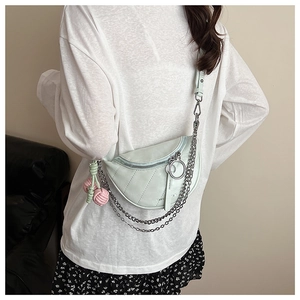 Dettaglio della borsa a sella verde menta con catene metalliche e ciondolo rosa su modella