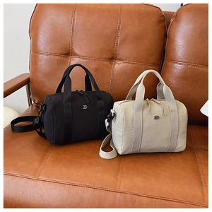 Détail des mini sacs Boston noir et beige avec double fermeture éclair sur un canapé