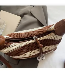 Close-up of smooth metal zipper and leather trim on a striped knit shoulder bag