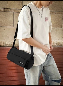 Gros plan d'un sac bandoulière cylindrique noir avec l'étiquette de marque DAMOSHU tissée