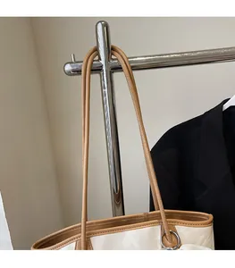 Dettaglio tracolla in pelle marrone con anelli in metallo argentato su borsa beige