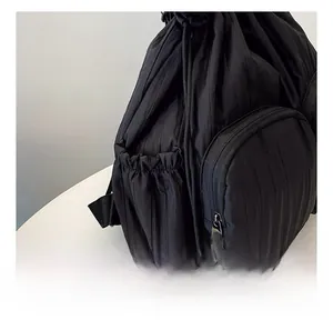 Macro view of black pleated nylon backpack showing drawstring side pocket and seam details