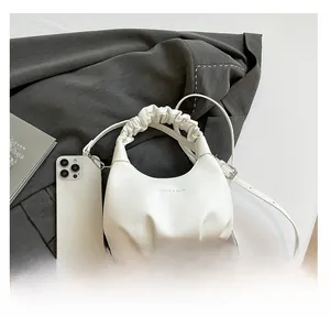 Close-up of white ruched leather handbag with embossed text and adjustable strap