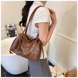Detailed view of brown leather crossbody bag with drawstring pleats and heart tag
