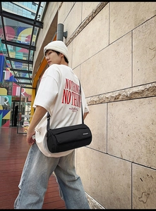 Photo street style d'un sac bandoulière cylindrique noir en tissu nylon imperméable