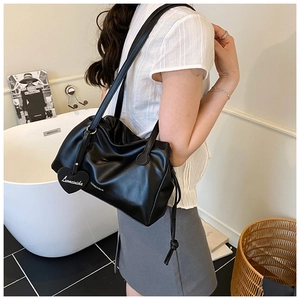 Detail of black pleated crossbody bag with heart charm and tassel, worn by model