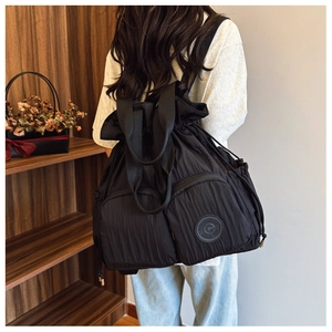Detail of black drawstring backpack showing pleated texture and brand logo patch