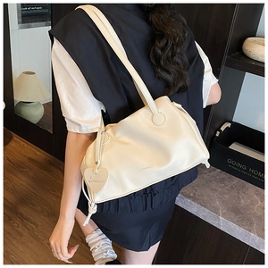 Detail view of beige ruched tote bag with heart pendant and brand logo on soft PU leather