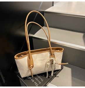 Dettaglio borsa sottobraccio marmorizzata crema con finiture in pelle marrone su un libro