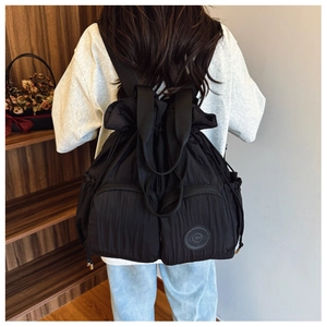 Detailed back view of a black drawstring backpack with unique vertical pleats and pockets