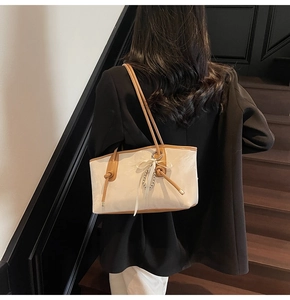 Dettaglio borsa tote crema con bordo marrone, fiocco in nastro e ciondolo di perle su blazer