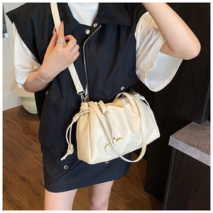Model view of beige pleated bucket bag with heart pendant and adjustable straps