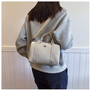 Vue détaillée d'une femme portant un sac bandoulière crème avec une sangle réglable