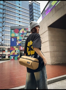 Gros plan d'un sac cylindrique kaki avec bandoulière noire réglable et détail logo