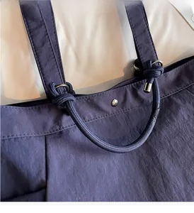 Detailed close-up of dark blue tote bag with knotted rope handle and metal hardware