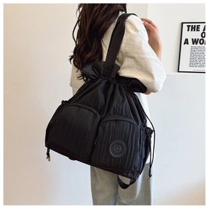 Side view of black nylon drawstring tote bag with dual front pockets on a model