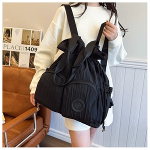Detail of black pleated nylon backpack featuring drawstring closure and functional front pockets