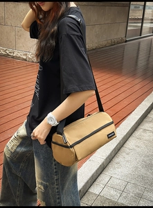 Gros plan du sac cylindrique en toile kaki avec bandoulière noire et étiquette