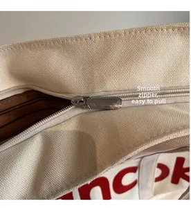 Detail of the smooth metal zipper and red letter print on the cream canvas tote bag