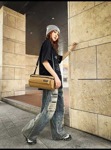 Gros plan du sac bandoulière cylindrique kaki porté avec une tenue de style streetwear